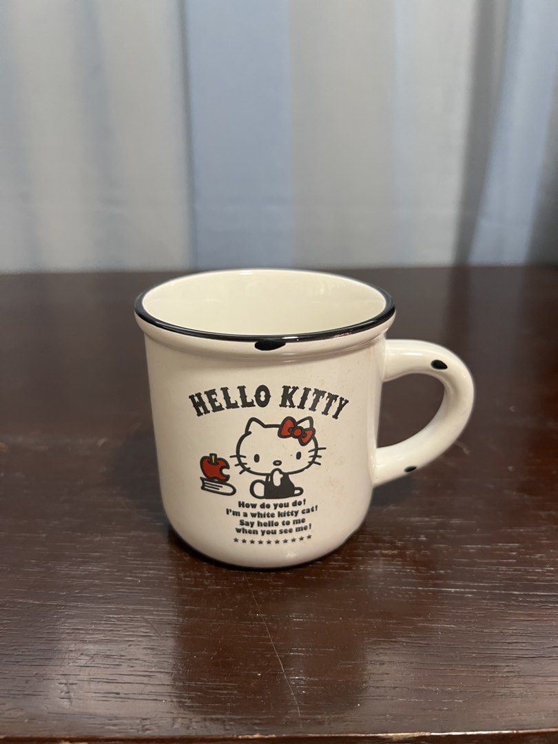Hello kitty cup (Category: Coffee & Tea Tableware) located in Manila. Submitted by rlab_japan_thrift (Listing ID 1462724708, Image 1). Description: Vintage-Style Sanrio Hello Kitty Enamelware-Look Ceramic Mug 🍎✨ An adorable retro-style ceramic mug designed to look like classic enamel campware with black trim detail! Features classic Hello Kitty artwork with her signature red bow, apples, and quote on both sides. * Design: Classic Hello Kitty wit