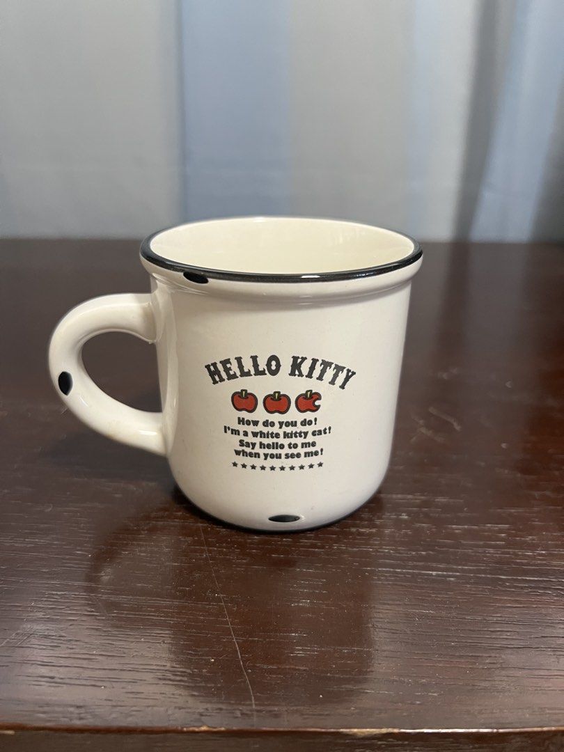 Hello kitty cup (Category: Coffee & Tea Tableware) located in Manila. Submitted by rlab_japan_thrift (Listing ID 1462724708, Image 2). Description: Vintage-Style Sanrio Hello Kitty Enamelware-Look Ceramic Mug 🍎✨ An adorable retro-style ceramic mug designed to look like classic enamel campware with black trim detail! Features classic Hello Kitty artwork with her signature red bow, apples, and quote on both sides. * Design: Classic Hello Kitty wit