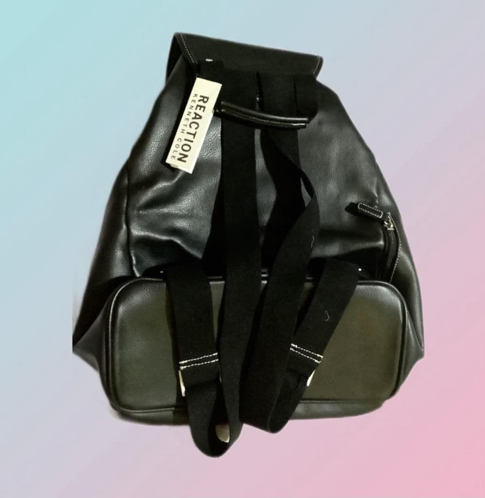 Kenneth Cole REACTION back pack (Category: Backpacks) located in Paranaque City. Submitted by calm_youngstore7 (Listing ID 1462813048, Image 2). Description: Kenneth Cole REACTION black faux-leather backpack featuring a classic drawstring main compartment under a magnetic flap closure and a distinctive silver square buckle accent. This specific design features a clean horizontal zippered pocket on the front lower body and a debossed "REACTION KEN