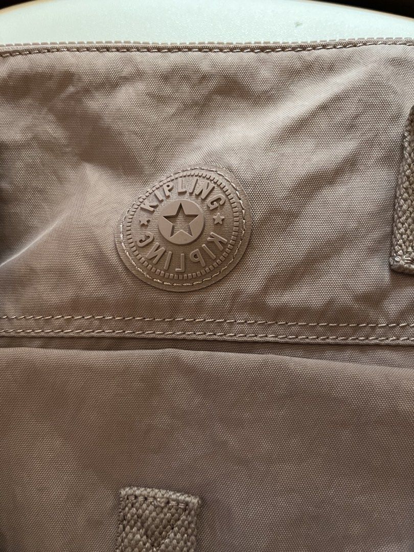 Kipling Tote Bag Taupe Nylon Shoulder Bag (Category: Tote Bags) located in Mandaluyong City. Submitted by yamcsf47597 (Listing ID 1462746387, Image 2). Description: - Taupe Kipling tote bag - Durable nylon material - Front pocket with snap closure - Adjustable shoulder strap - Silver-toned zippers and hardware - Iconic Kipling logo on the front - Ideal for everyday use.