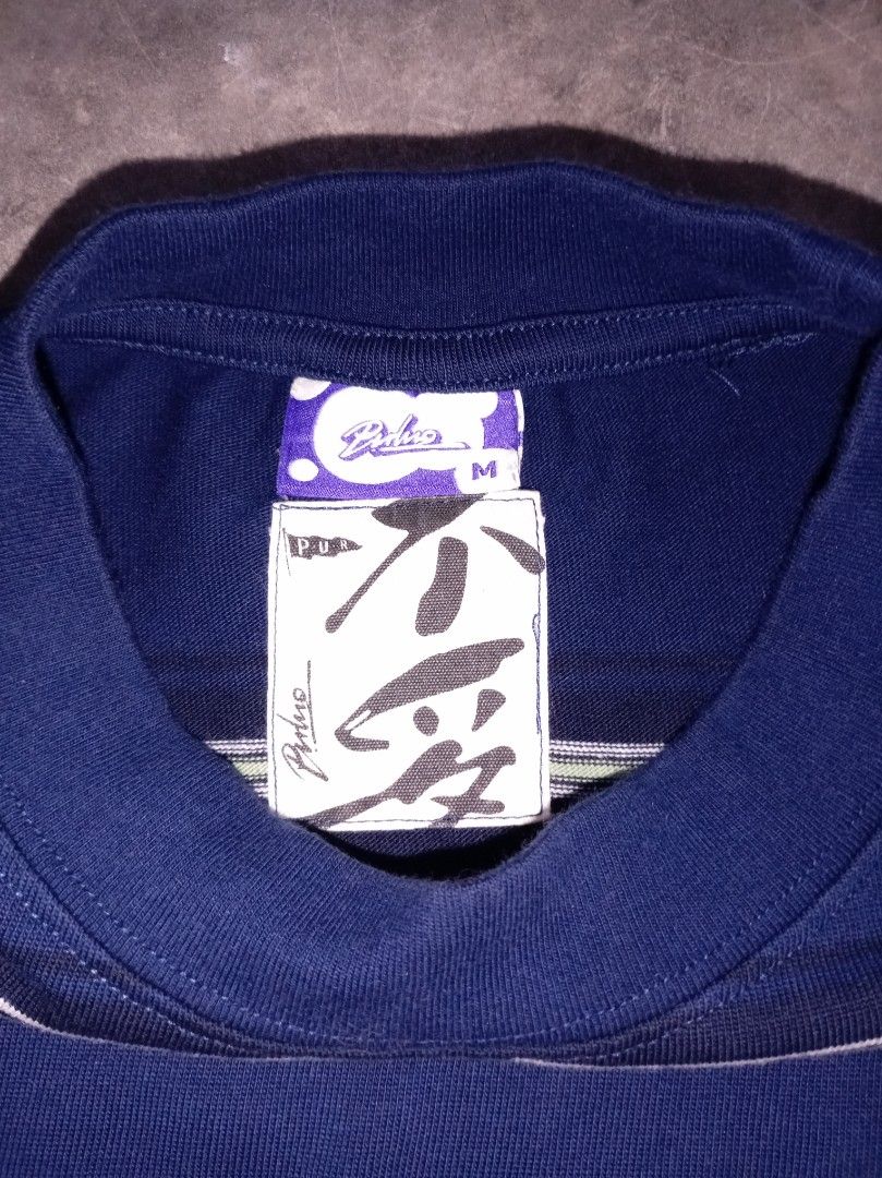 PULUTO Striped T-shirt Size M (Category: Tshirts & Polo Shirts ) located in Nagcarlan. Submitted by asd0606 (Listing ID 1462855449, Image 3). Description: - Navy blue t-shirt with horizontal stripes - Stripe colors: Purple, White, Grey - Short sleeves and crew neck design - Embroidered PULUTO logo on chest - Small tag detail on the hem - Made from 100% cotton fabric - Ideal for everyday casual wear.