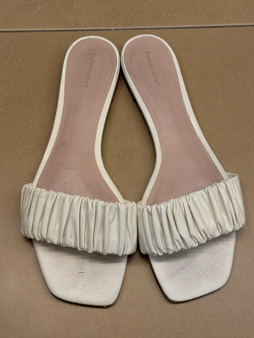 Reformation White Ruched Slide Sandals (Category: Flats & Sandals) located in Makati City. Submitted by sellebrity88 (Listing ID 1462713430, Image 1). Description: - Brand: Reformation US 9 - Color: White - Style: Slide Sandals - Features: Ruched strap, square toe, slip-on design - Occasion: Casual wear - Condition: Good, with some signs of wear on the soles.