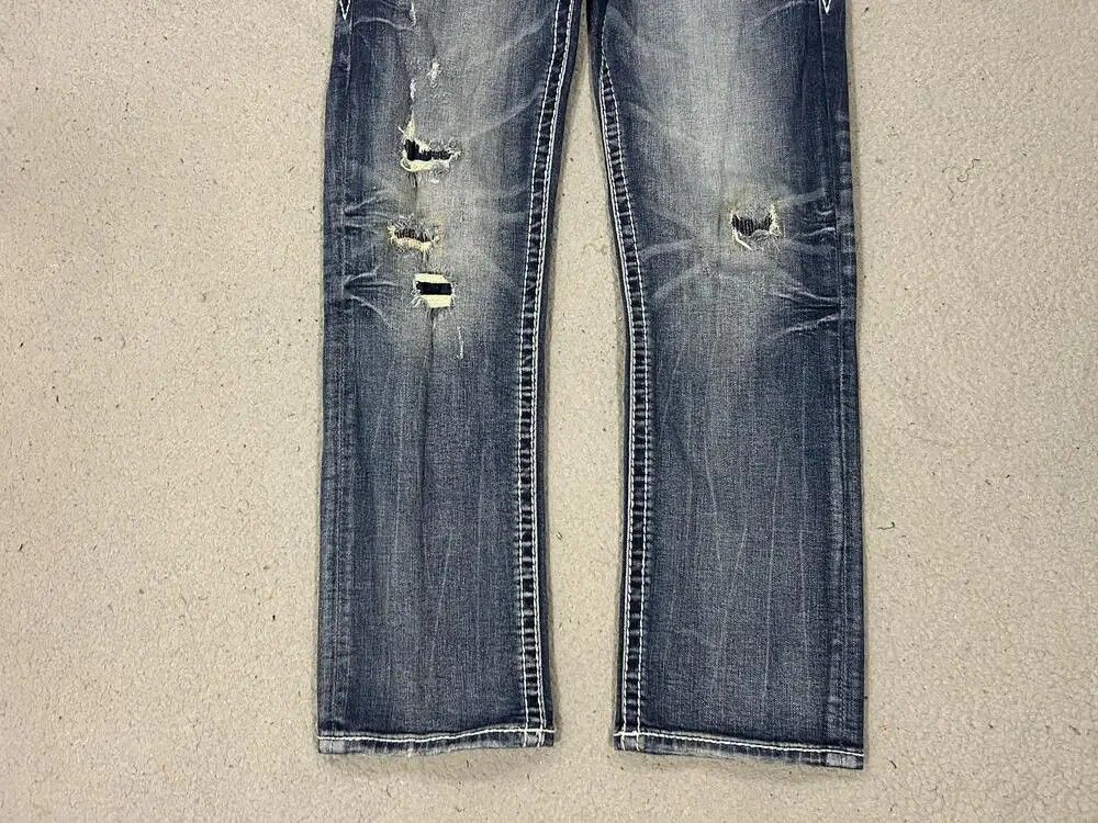 Rock Revival Jeans Distressed Blue Denim (Category: Jeans) located in Caloocan City. Submitted by thriftnigab2 (Listing ID 1462869122, Image 3). Description: - Rock Revival jeans - Distressed blue wash - White contrast stitching - Signature Rock Revival logo on back pockets - Rips and wear on front - Designed in USA, Made in Vietnam - Perfect for casual wear.