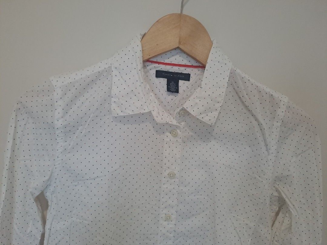 Tommy Hillfiger longsleve (Category: Longsleeves) located in Manila. Submitted by joanbalde39643 (Listing ID 1462778213, Image 2). Description: The image shows a Tommy Hilfiger women's white long-sleeve button-down shirt featuring a subtle all-over dark polka dot or micro-print pattern. It features a classic pointed collar, a central button placket, long sleeves with buttoned cuffs, and the signature tiny Tommy Hilfiger flag logo embroidered on t