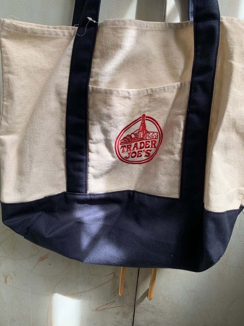 Trader Joe's Canvas Tote Bag (Category: Tote Bags) located in Manila. Submitted by usagichan_rabbit (Listing ID 1462815216, Image 2). Description: - Classic Trader Joe's canvas tote bag - Color: Beige with navy blue bottom and straps - Features a front pocket with embroidered logo - Ideal for groceries or everyday use - Made with durable material -Preloved but needs washing, bought from US.