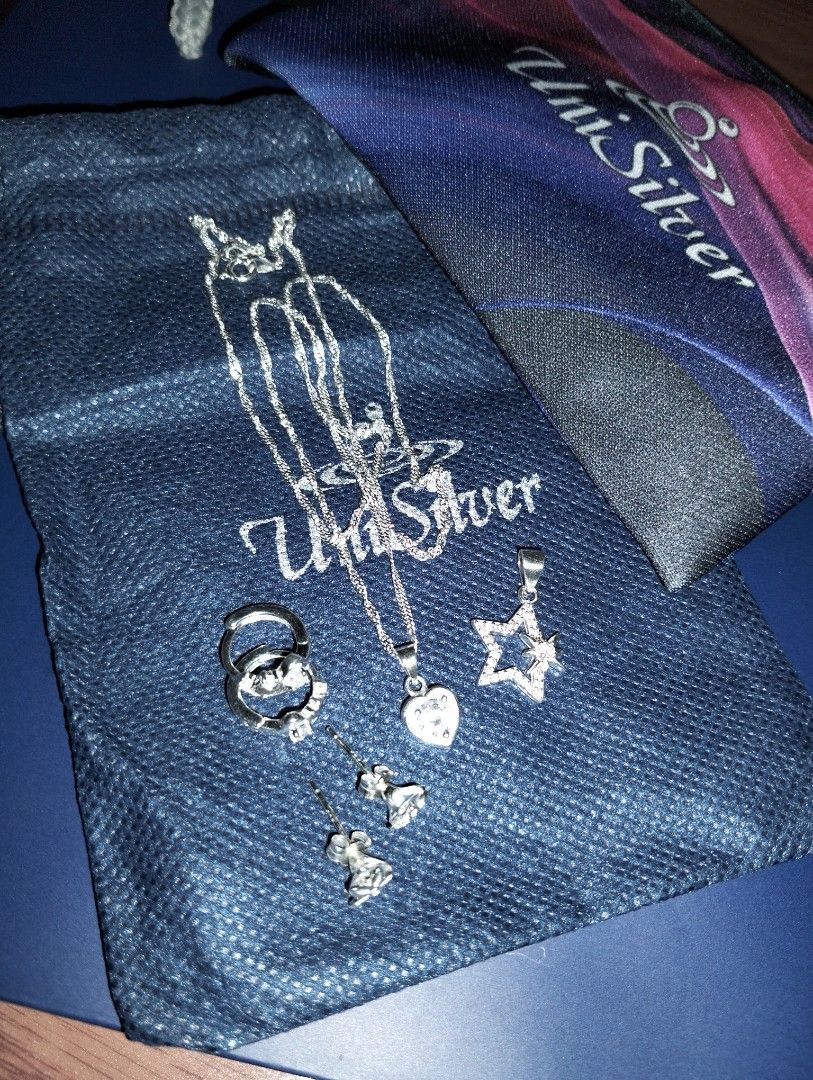 UniSilver Necklace and Earrings (Category: Necklaces) located in Caloocan City. Submitted by girlshopmcollection (Listing ID 1462866487, Image 1). Description: - Authentic UniSilver jewelry set - Includes: delicate chain necklace with heart pendant, pair of stud earrings, pair of hoop earrings, and a star pendant - Embellishments: Cubic zirconia stones - Packaging: Comes with a blue pouch and a colorful fabric bag.