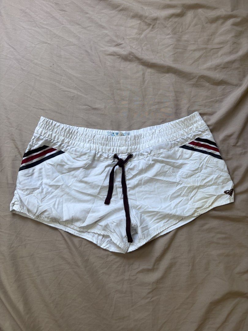 vintage Roxy White Beach surf shorts (Category: Bikinis & Swimsuits) located in Andop. Submitted by ukaylangpo (Listing ID 1462770112, Image 2). Description: - Roxy swim shorts - Size: Medium (M) - Elastic waistband with adjustable drawstring - Features red and navy stripe detail on sides and back - Small Roxy logo on the front - Material: 100% Polyester - Ideal for beach or pool activities.