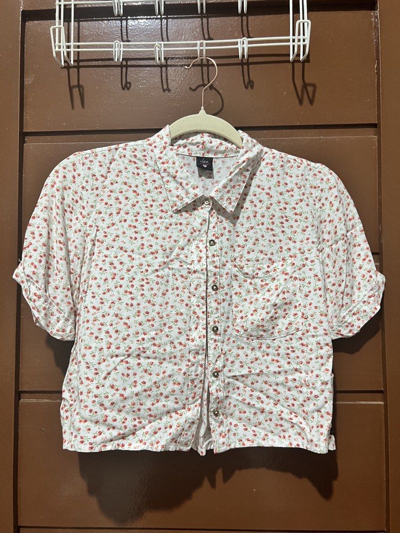 White Floral Button-Up Shirt (Category: Shirts) located in Binan City. Submitted by closet_in_disguise (Listing ID 1462692325, Image 1). Description: - Cute white shirt - Small red floral print - Short sleeves with rolled cuffs - Button-up front - Left chest pocket - Pairs well with jeans or shorts - Lightweight fabric, ideal for warm weather.