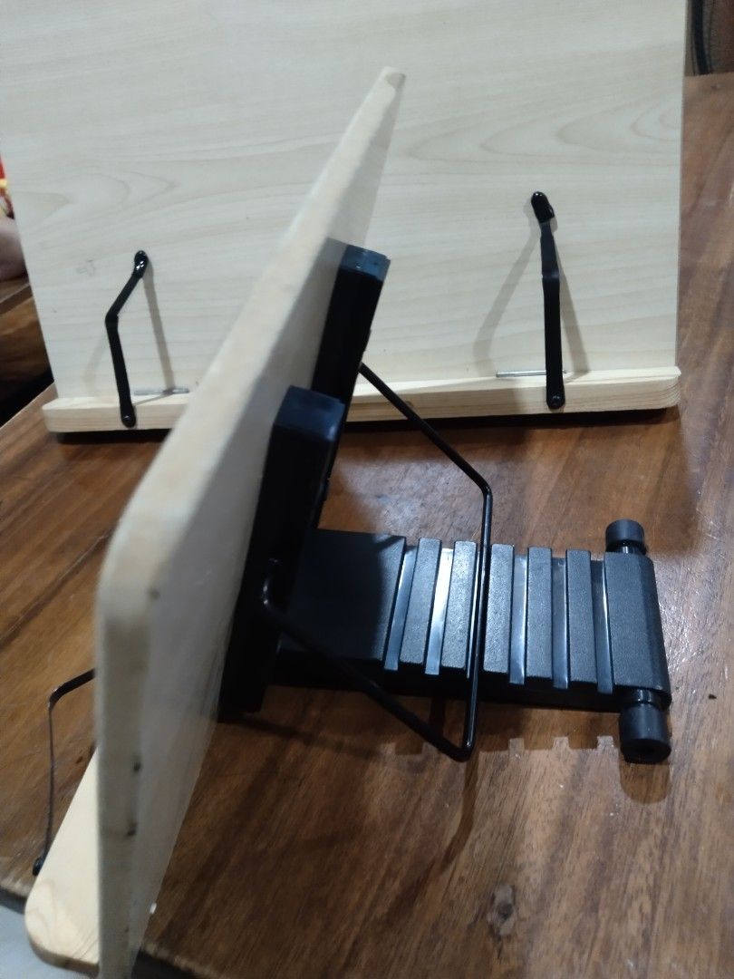 Wooden Book Stand with Adjustable Metal Support (Category: Office Furniture & Fixtures) located in Cavite. Submitted by dimple082 (Listing ID 1462786663, Image 2). Description: - Set of 2 wooden book stands - Light-colored wood - Adjustable black metal supports on both stands - Ideal for holding books or tablets - Folds flat for convenient storage - Perfect for desks, kitchen counters, or any workspace.