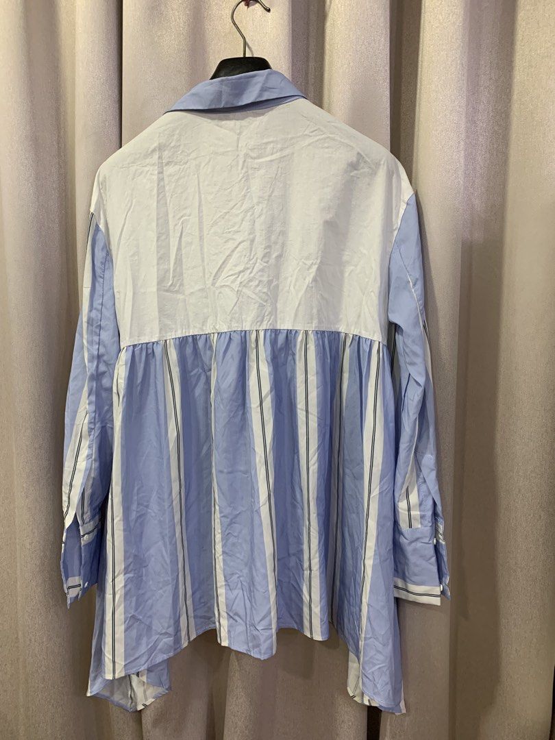 Blue and White Striped Asymmetrical Button-Up Shirt (Category: Shirts) located in Pasig City. Submitted by angelamendozaaa (Listing ID 1459134479, Image 3). Description: - Cool blue and white vertical stripes - Asymmetrical hemline for a modern look - Classic button-up front and collar - Long sleeves with button cuffs - Unique pleated detail on the front - Versatile for casual or smart-casual outfits.