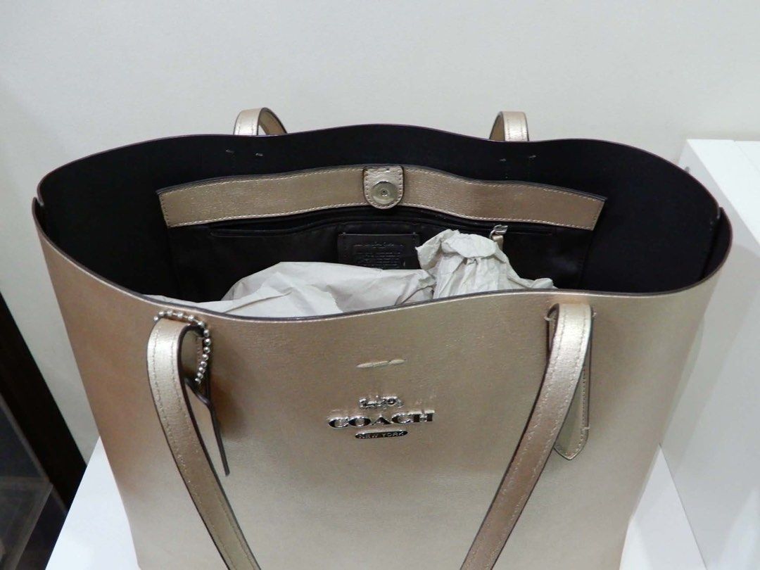 Coach Metallic Gold Leather Tote Bag (Category: Luxury Bags & Wallets) located in Las Pinas. Submitted by Itanz (Listing ID 1459230567, Image 3). Description: - Authentic Coach tote bag in stunning metallic gold. - Spacious interior with multiple compartments: 1 zip pocket and 1 snap closure pocket. - Premium leather exterior featuring the iconic Coach New York logo. - Comfortable and sturdy handles for easy carrying. - Versatile design, ideal fo