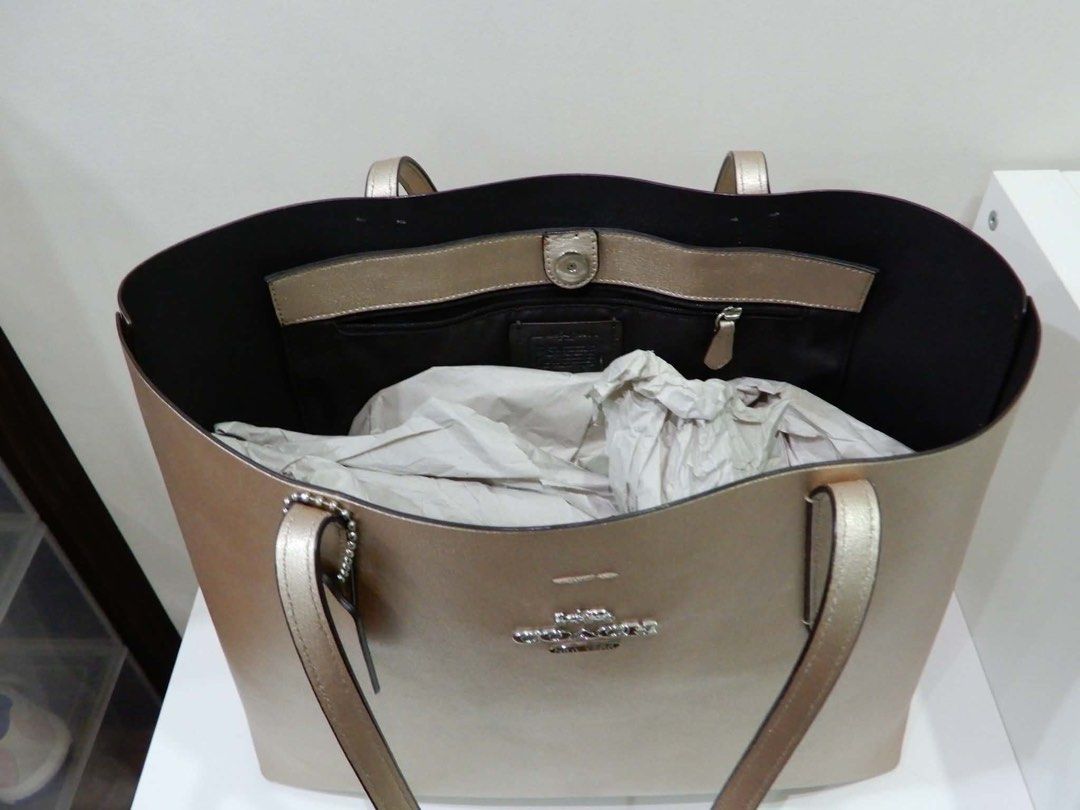 Coach Metallic Gold Leather Tote Bag (Category: Luxury Bags & Wallets) located in Las Pinas. Submitted by Itanz (Listing ID 1459230567, Image 2). Description: - Authentic Coach tote bag in stunning metallic gold. - Spacious interior with multiple compartments: 1 zip pocket and 1 snap closure pocket. - Premium leather exterior featuring the iconic Coach New York logo. - Comfortable and sturdy handles for easy carrying. - Versatile design, ideal fo