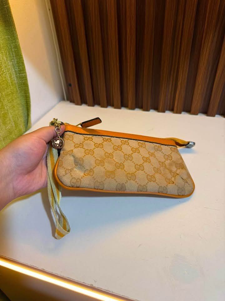 Gucci GG Monogram Canvas Pouch Wristlet (Category: Luxury Bags & Wallets) located in Los Banos. Submitted by ukaynidizkie (Listing ID 1459215034, Image 3). Description: - Gucci pouch - Classic GG monogram canvas - Tan and orange leather trim - Includes wrist strap - Features chain detail - Secure zipper closure - Ideal for carrying your essentials.