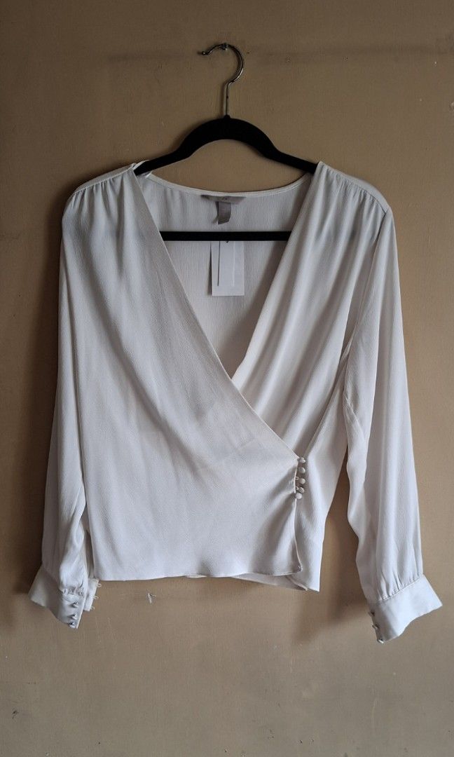 H&M Off White Blouse (Category: Blouses) located in Manila. Submitted by thrifter_lifestyle (Listing ID 1459098553, Image 1). Description: Brand: H&M Long sleeves, button on wrists Wrap style, button mechanism to close in front V Neck Material: Polyester (see tag) Fabric is silk like and flowy. Added close up photos for appreciation. 🙂 Actual Color: Off White/Light Ecru Bust: 40" Length (shoulder to waist): 22" No issues, never worn. With tag, s