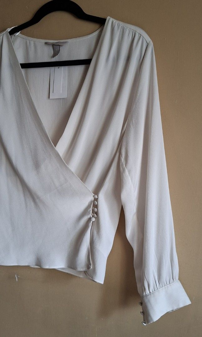 H&M Off White Blouse (Category: Blouses) located in Manila. Submitted by thrifter_lifestyle (Listing ID 1459098553, Image 3). Description: Brand: H&M Long sleeves, button on wrists Wrap style, button mechanism to close in front V Neck Material: Polyester (see tag) Fabric is silk like and flowy. Added close up photos for appreciation. 🙂 Actual Color: Off White/Light Ecru Bust: 40" Length (shoulder to waist): 22" No issues, never worn. With tag, s