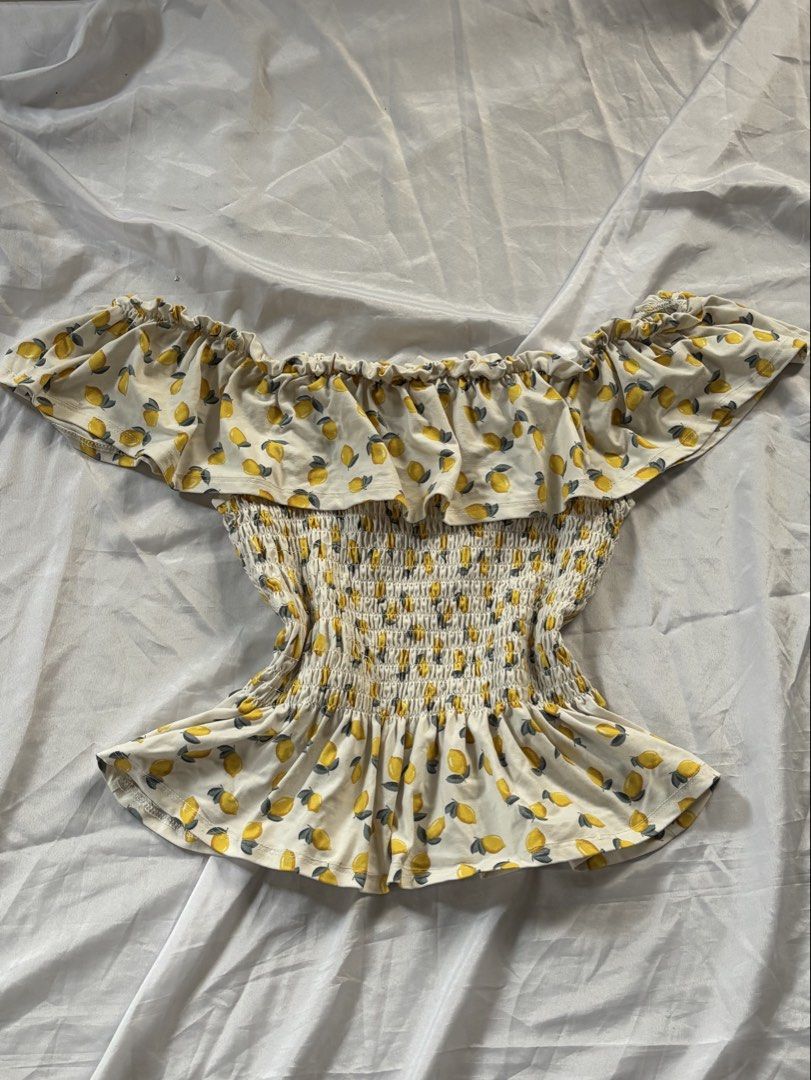 Off-Shoulder Smocked Top (Category: Sleeveless) located in Cabuyao City. Submitted by allysanikoru (Listing ID 1459239252, Image 1). Description: Size: Small to Medium (Stretchable) Color: Off-White with Lemon Print Details: Off-shoulder neckline with ruffled trim, fully smocked bodice, peplum hem.