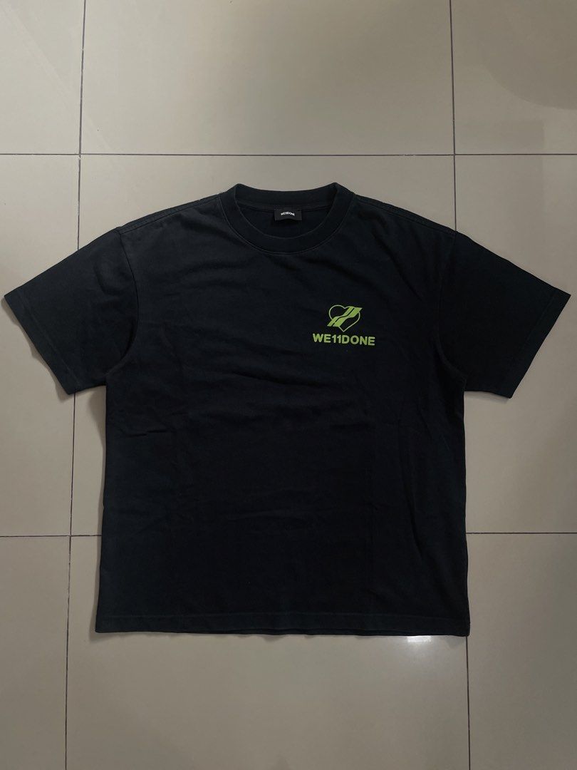 WE11DONE Black T-shirt with Heart Graphic (Category: Tshirts & Polo Shirts ) located in Pili. Submitted by samskolekta_12. (Listing ID 1459242321, Image 1). Description: - Brand: WE11DONE - Color: Black - Size: S - Front Detail: Neon green logo - Back Detail: Large heart graphic with repeated brand name - Condition: Good, no major flaws .