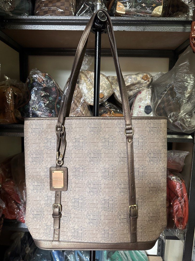 Anne Klein Tote Bag (Category: Tote Bags) located in Butuan. Submitted by slownsteady_ (Listing ID 1463005155, Image 1). Description: - Brand: Anne Klein New York - Style: Tote Bag - Color: Beige with all-over logo print - Accents: Bronze trim and straps - Exterior: Zippered front pocket - Interior: Main compartment with interior zip pocket - Extras: Matching logo charm - Perfect for the office.