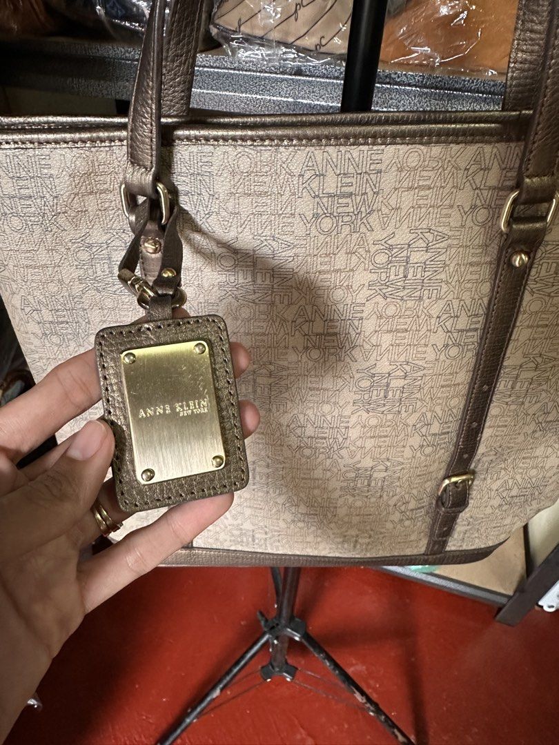 Anne Klein Tote Bag (Category: Tote Bags) located in Butuan. Submitted by slownsteady_ (Listing ID 1463005155, Image 2). Description: - Brand: Anne Klein New York - Style: Tote Bag - Color: Beige with all-over logo print - Accents: Bronze trim and straps - Exterior: Zippered front pocket - Interior: Main compartment with interior zip pocket - Extras: Matching logo charm - Perfect for the office.