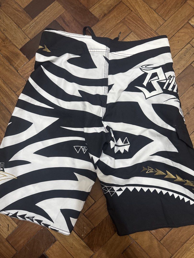 Billabong Board Shorts (Category: Shorts) located in Manila. Submitted by mabuhaymiles (Listing ID 1463037684, Image 3). Description: - Brand: Billabong - Size: 12 - Design: Black and white tribal print with gold accents - Material: 100% Polyester - Closure: Lace-up front - Features: Back pocket with velcro closure - Ideal for: Swimming, surfing, or beach activities.