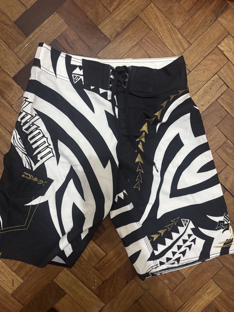Billabong Board Shorts (Category: Shorts) located in Manila. Submitted by mabuhaymiles (Listing ID 1463037684, Image 1). Description: - Brand: Billabong - Size: 12 - Design: Black and white tribal print with gold accents - Material: 100% Polyester - Closure: Lace-up front - Features: Back pocket with velcro closure - Ideal for: Swimming, surfing, or beach activities.
