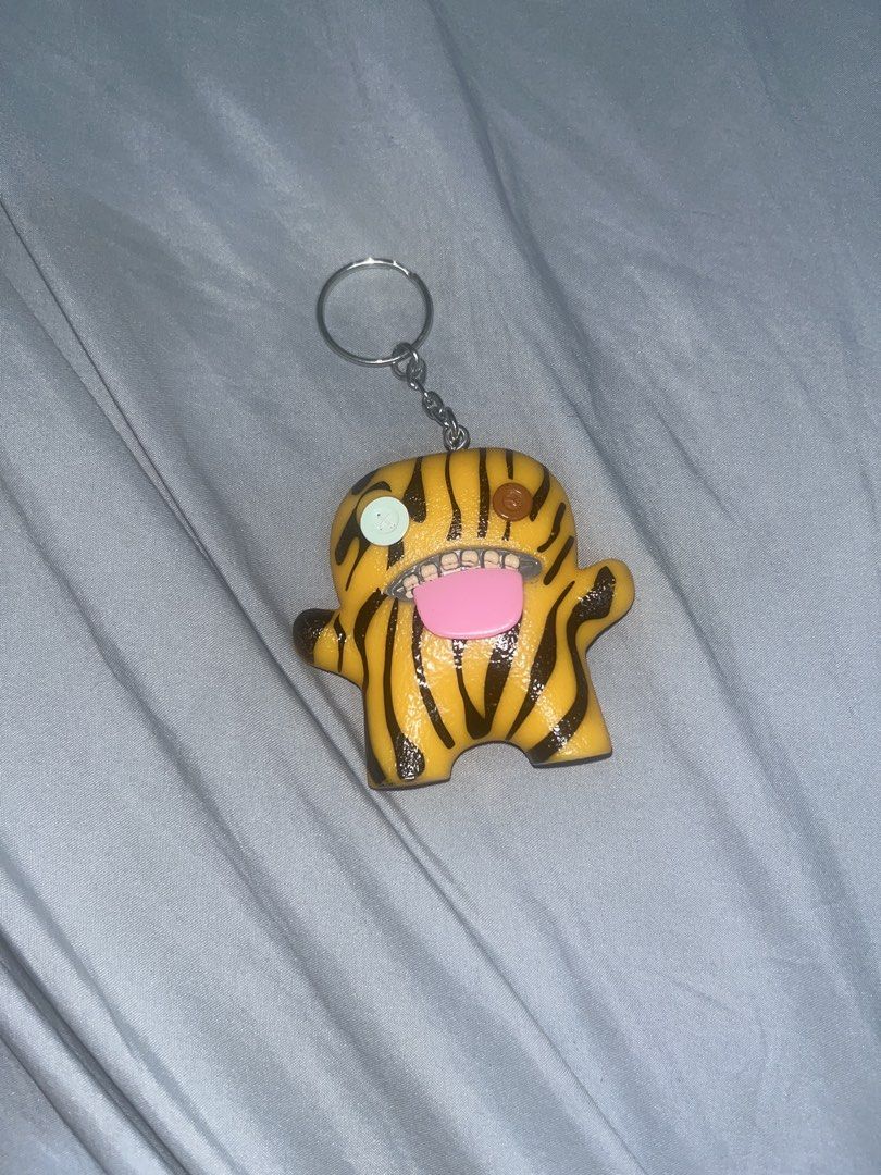 Fuggler Keychain (Category: Plushies & Soft Toys) located in Paranaque City. Submitted by goldenwolf28 (Listing ID 1463058570, Image 1). Description: - Adorable tiger-striped Domo-kun keychain - Features a cute pink tongue and big teeth - Unique mismatched eyes: one light blue, one brown - Perfect accessory for bags, backpacks, or keys - Adds a fun and quirky touch to your style Reason for selling: decluttering.