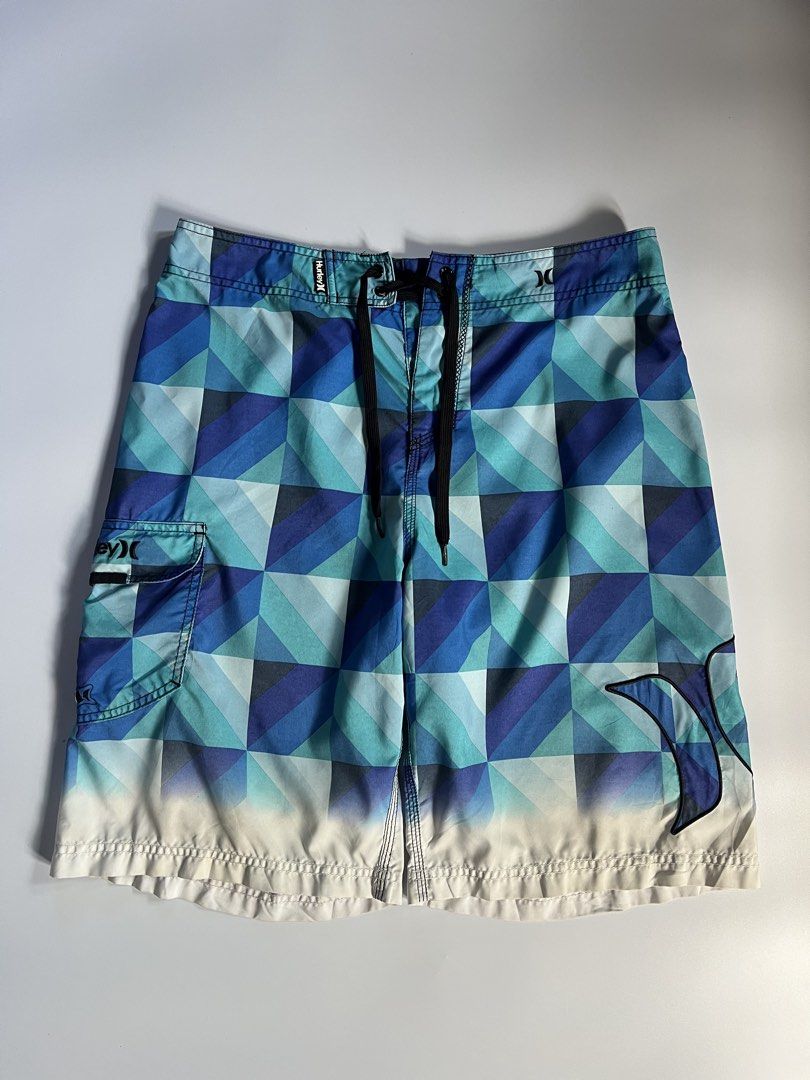 Hurley Geometric Print Board Shorts Blue (Category: Swim Trunks & Board Shorts) located in Baler. Submitted by allthrifted31 (Listing ID 1462962890, Image 1). Description: - Cool Hurley board shorts - Geometric pattern in shades of blue and teal - Side cargo pocket with velcro closure - Drawstring waist for adjustable fit - Ideal for beach or pool activities.