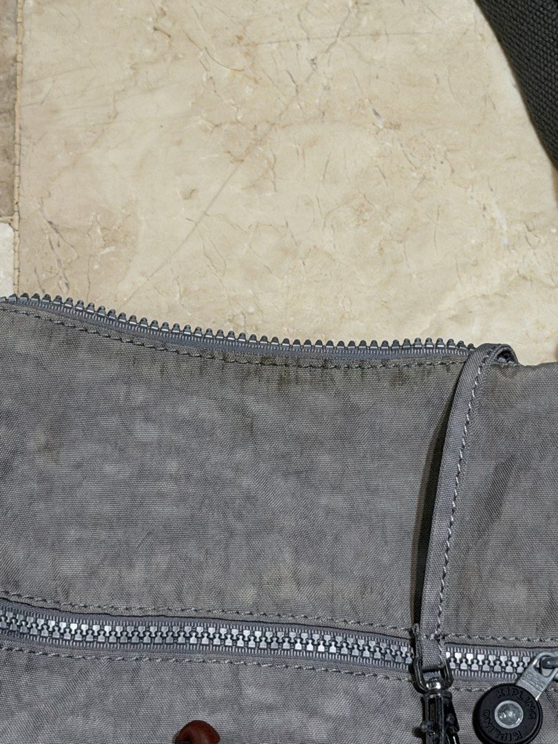 Kipling Grey Nylon Crossbody Bag with Monkey Charm (Category: Cross-body Bags) located in Manila. Submitted by db_collective (Listing ID 1462987089, Image 3). Description: - Grey Kipling crossbody bag - Durable nylon material - Front zipper pocket - Main zipper compartment - Adjustable strap for comfort - Includes signature Kipling monkey charm - Ideal for everyday use - Shows some signs of wear, especially around zipper areas and hardware Please
