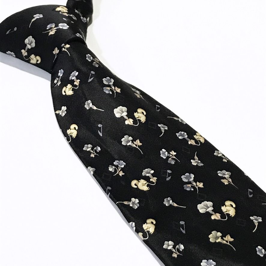 Nicole Miller Black Floral Pattern Neck Tie (Category: Ties) located in Taguig. Submitted by retrogaze (Listing ID 1463042067, Image 1). Description: This 100% silk necktie by Nicole Miller features a solid black base with a smooth, soft-sheen finish. The body displays a charming novelty pattern of delicate mini floral blossoms in periwinkle blue and cream, interspersed with small beige squirrels and floating musical notes. Brand Overview: Nicole
