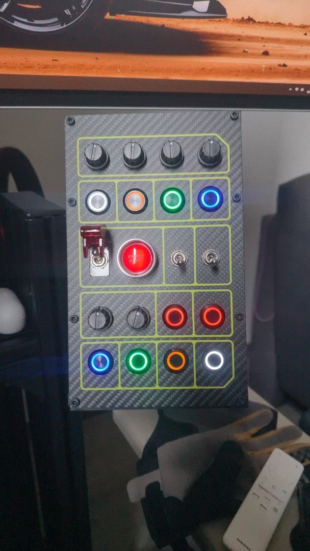 Sim Racing Button Box with Knobs and Switches (Category: Controllers) located in Kuala Lumpur. Submitted by grandwolf_0287a2 (Listing ID 1462936356, Image 1). Description: - Custom-built sim racing button box - Multiple illuminated buttons (Red, Green, Blue, White, Orange) - Toggle switches for added control - Prominent red emergency stop button - Sleek carbon fiber look with yellow trim - Enhances your sim racing experience - Easy USB connection