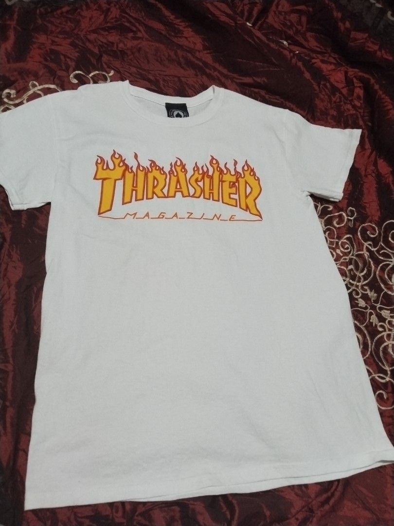 Thrasher White Tee (Category: Tshirts & Polo Shirts ) located in Mabalacat. Submitted by al_amin_thrift (Listing ID 1463028976, Image 1). Description: - Brand: Thrasher — Iconic Skateboarding Magazine ​ - Origin: San Francisco, USA ​ - Color: White with Classic Yellow/Orange Flame Logo ​ - Size: S (P/CH) — Standard Small ​ - Fabric: 100% Cotton — soft & durable ​ - Made in: Nicaragua ​ - Design: "Thrasher" flame lettering + "MAGAZINE" underline ​