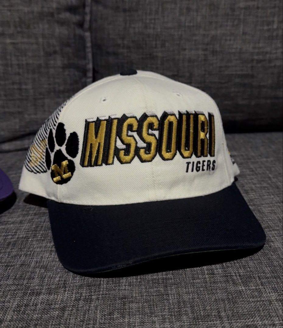 Vintage Missouri Tigers Shadow Cap (Category: Caps & Hats) located in Solano. Submitted by Hustle.Everyday (Listing ID 1463038169, Image 1). Description: - Embroidered 'MISSOURI' and 'TIGERS' in gold and black - Features paw print and 'M' logo on the side - Adjustable snap at the back - Ideal for any Missouri Tigers fan.