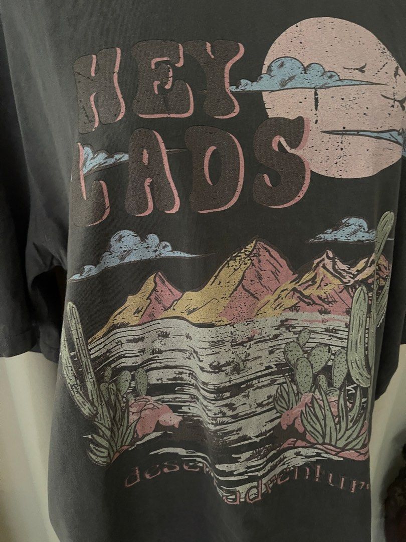 acidwash Gray-pink vintagey (Category: Shirts) located in Cainta. Submitted by zlove111 (Listing ID 1463178679, Image 3). Description: - Cool grey oversized graphic t-shirt - Features a desert landscape design with mountains, cacti, and a moon - Text reads 'HEY LADS' and 'DESERT ADVENTURE' - Unique light pink trim around the neckline - Oversized fit for a relaxed, casual style - Ideal for everyday wear and adding a touch of adventure to your look