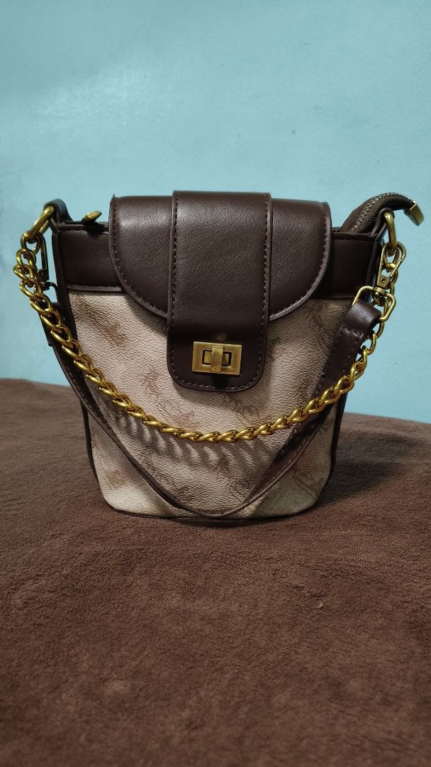 Brown and beige patterned bucket bag with gold chain strap (Category: Cross-body Bags) located in Manila. Submitted by serenitycarlylle (Listing ID 1463302127, Image 1). Description: - Adorable bucket bag with a stylish patterned body. - Chic brown trim and secure flap closure. - Elegant gold chain strap for comfortable carrying. - Includes a convenient zippered compartment inside. - Ideal for everyday use, fitting all your essentials..