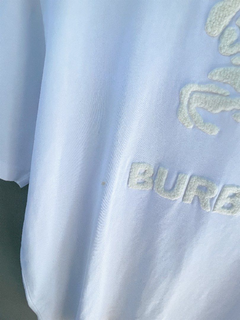 Burberry White Embossed Logo T-Shirt (Category: Tshirts & Polo Shirts ) located in San Nicolas. Submitted by .luxfinds_0222 (Listing ID 1463319369, Image 3). Description: Size: L-XL Width :23 Length :28 CR:9.5 Issue minimal stain/repair pinhole - Burberry T-shirt - Size L (based on tag) - Features embossed Horseferry print and logo - Short sleeves, crew neck - Small repair pinhole on front (refer to last photo).