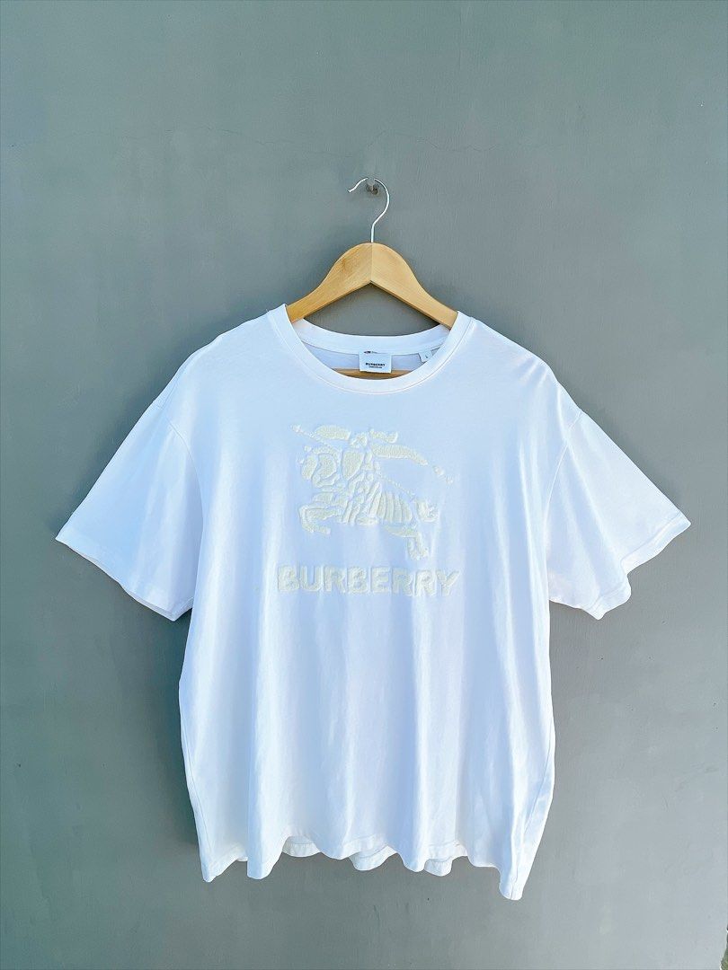 Burberry White Embossed Logo T-Shirt (Category: Tshirts & Polo Shirts ) located in San Nicolas. Submitted by .luxfinds_0222 (Listing ID 1463319369, Image 1). Description: Size: L-XL Width :23 Length :28 CR:9.5 Issue minimal stain/repair pinhole - Burberry T-shirt - Size L (based on tag) - Features embossed Horseferry print and logo - Short sleeves, crew neck - Small repair pinhole on front (refer to last photo).