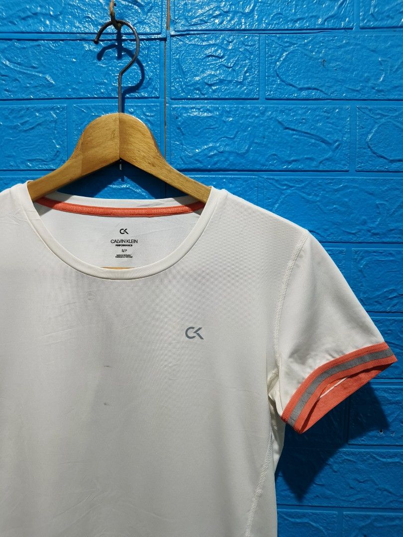 Calvin Klein Performance White T-shirt Size S (Category: Activewear) located in Davao. Submitted by vndrgd (Listing ID 1463119946, Image 3). Description: - White Calvin Klein Performance T-shirt - Size: S - Orange trim on sleeves and neckline - Measurements: 17" width, 24" length - Minor faint marks on front and near hem - Perfect for workouts or casual wear.