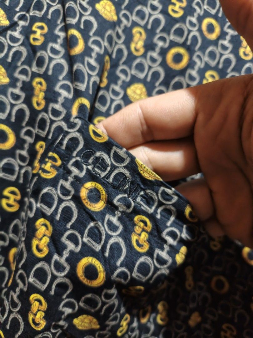 CELINE All Over Print Polo Shirt (Category: Tshirts & Polo Shirts ) located in Maasim. Submitted by ukayganda25 (Listing ID 1463299598, Image 2). Description: - Classic CELINE polo shirt - Iconic all-over print featuring horseshoe and 'CELINE PARIS' motifs - Dark navy base with elegant gold and grey details - Black collar and button-up front - Perfect for a stylish casual look - Attention to detail on buttons and print.
