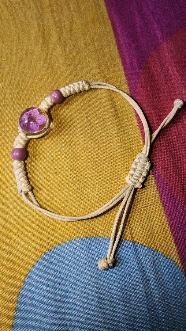 Handmade Bracelet with Purple Flower Charm (Category: Bracelets) located in Manila. Submitted by rare.elieli (Listing ID 1463169764, Image 1). Description: - Handmade bracelet - Features a clear bead with a real purple flower inside - Macrame cord with purple bead accents - Adjustable tie closure - Ideal for everyday wear or as a gift.