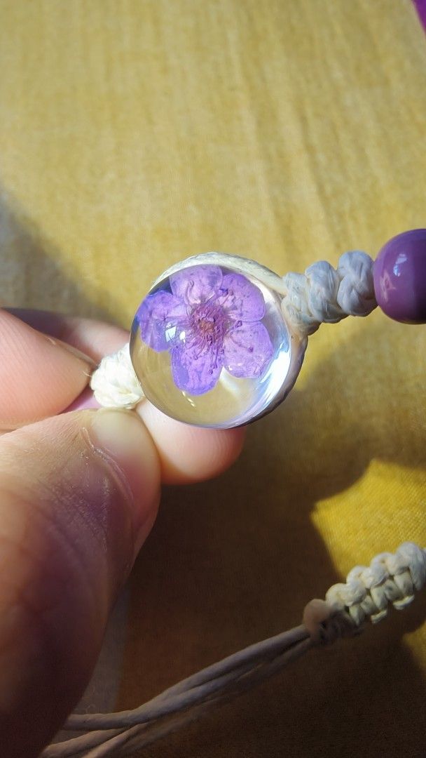 Handmade Bracelet with Purple Flower Charm (Category: Bracelets) located in Manila. Submitted by rare.elieli (Listing ID 1463169764, Image 2). Description: - Handmade bracelet - Features a clear bead with a real purple flower inside - Macrame cord with purple bead accents - Adjustable tie closure - Ideal for everyday wear or as a gift.