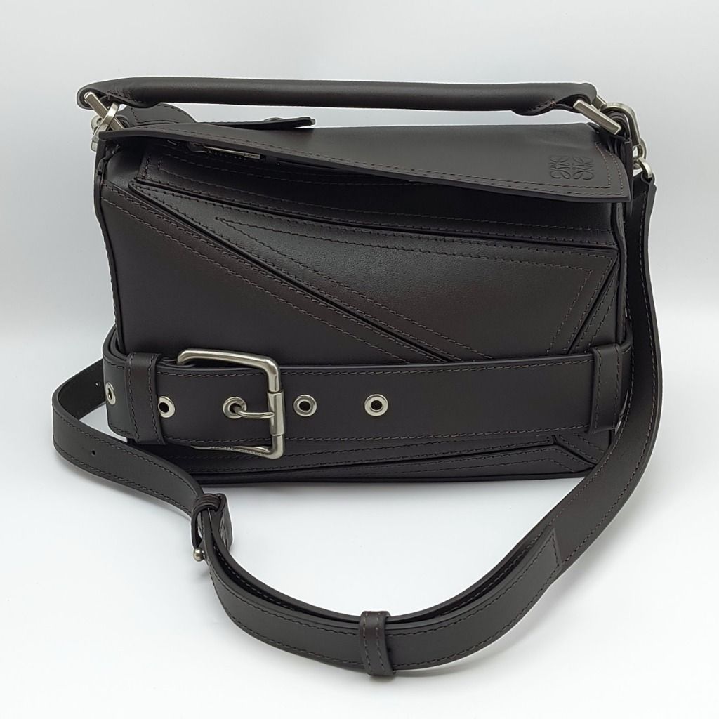 Loewe Puzzle Biker Small Bag Dark Brown (Category: Luxury Bags & Wallets) located in Cebu City. Submitted by theluxxaffair (Listing ID 1463298622, Image 2). Description: Loewe Puzzle Biker Small bag in dark brown shiny calfskin leather with silver-tone hardware. Features the signature Puzzle construction, biker-inspired buckle belt, top handle and detachable shoulder strap. Finished with zip closure and embossed Loewe Anagram logo. Length: 25 cm 