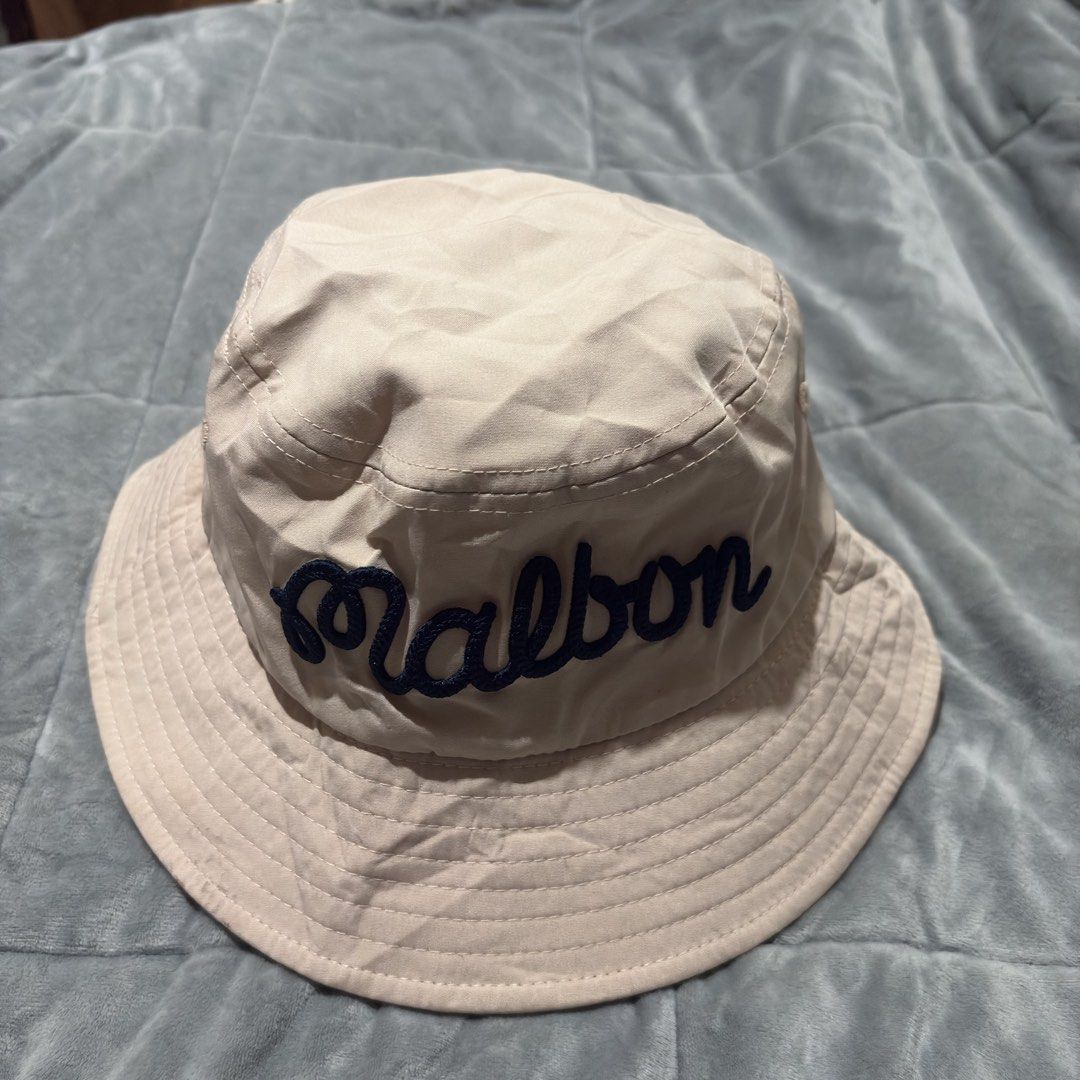 Malbon Golf Bucket Hat - Beige (Category: Caps & Hats) located in Carmen. Submitted by rr_thrifts (Listing ID 1463273450, Image 2). Description: - Cool Malbon bucket hat - Beige color with navy blue embroidery - Malbon logo on the front - Fun golf graphic on the side - Ideal for sunny days, on or off the golf course - One size fits most.