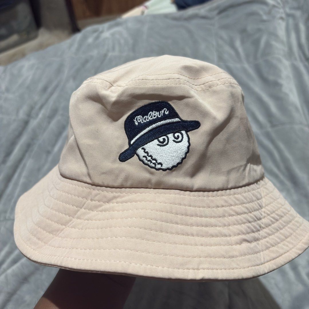 Malbon Golf Bucket Hat - Beige (Category: Caps & Hats) located in Carmen. Submitted by rr_thrifts (Listing ID 1463273450, Image 3). Description: - Cool Malbon bucket hat - Beige color with navy blue embroidery - Malbon logo on the front - Fun golf graphic on the side - Ideal for sunny days, on or off the golf course - One size fits most.