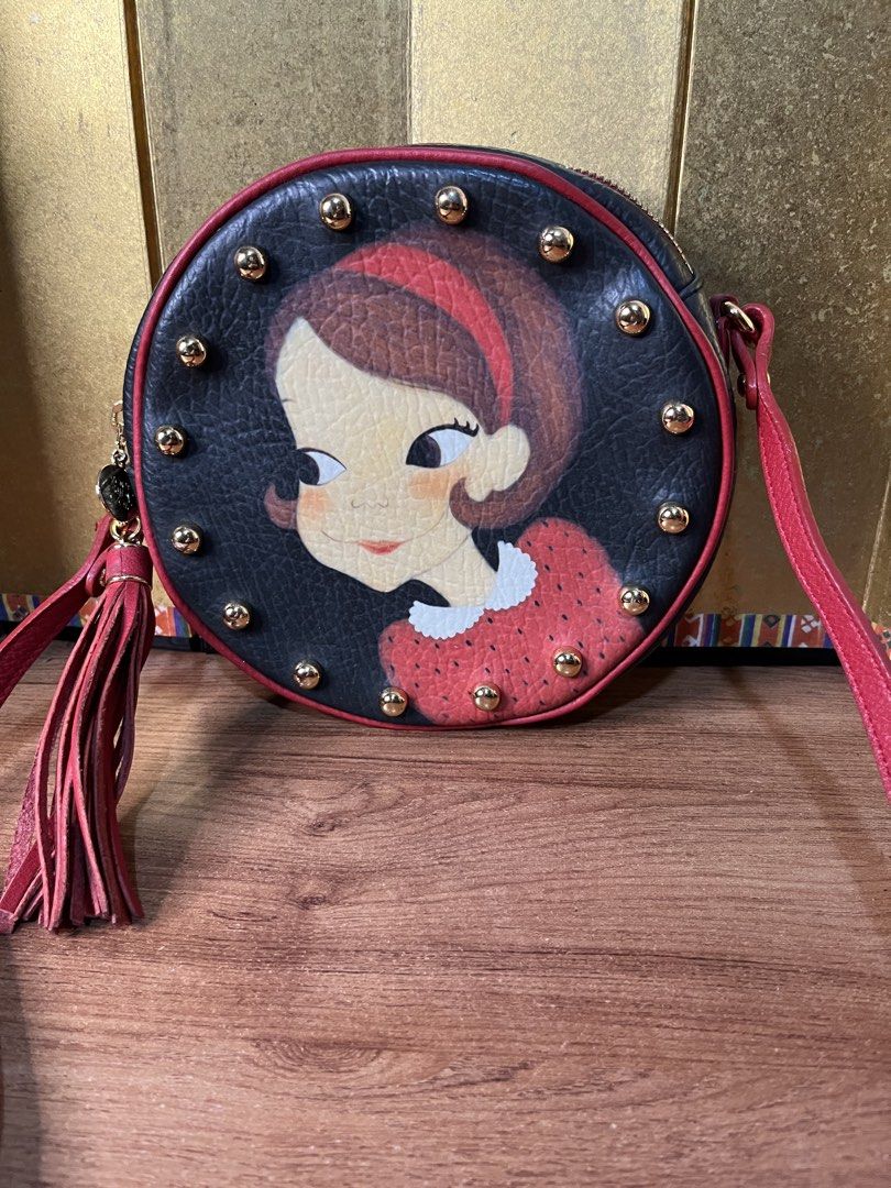 Original YOUK SHIM WON Sling Bag (Category: Cross-body Bags) located in Gapan. Submitted by lunashop14 (Listing ID 1463145084, Image 2). Description: Collector’s piece! 🎨✨ Selling this gorgeous authentic Youk Shim Won round crossbody bag. It features the brand’s iconic, playful character portrait framed by edgy gold-toned studs and a statement red leather tassel. Perfect for adding a pop of color and artistic flair to any outfit.🎒 Compact round