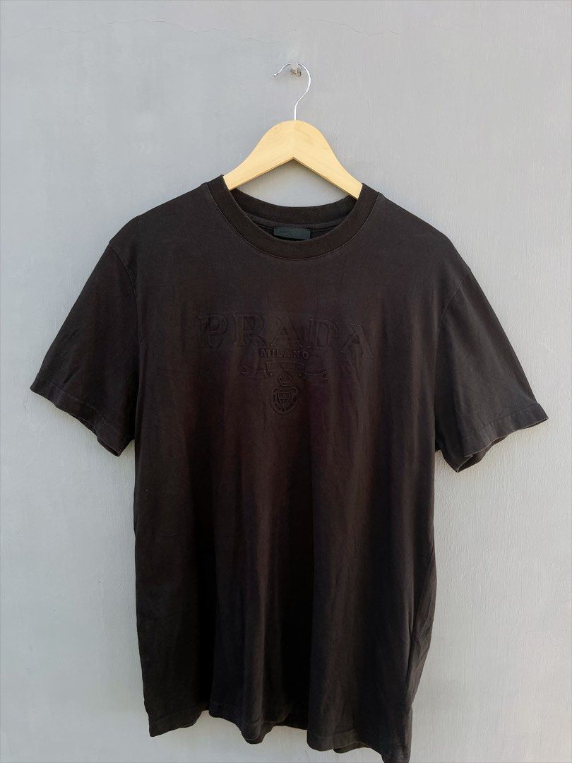 Prada Milano Embossed Logo T-Shirt Black (Category: Luxury Apparel) located in San Nicolas. Submitted by .luxfinds_0222 (Listing ID 1463322346, Image 1). Description: Size: M-L Width :21 Length :27.5 CR:9/10 Issue :NONE - Authentic Prada T-Shirt - Color: Black - Features embossed Prada logo, 'Prada Milano', and crest design - Made in Italy - Ideal for casual wear.