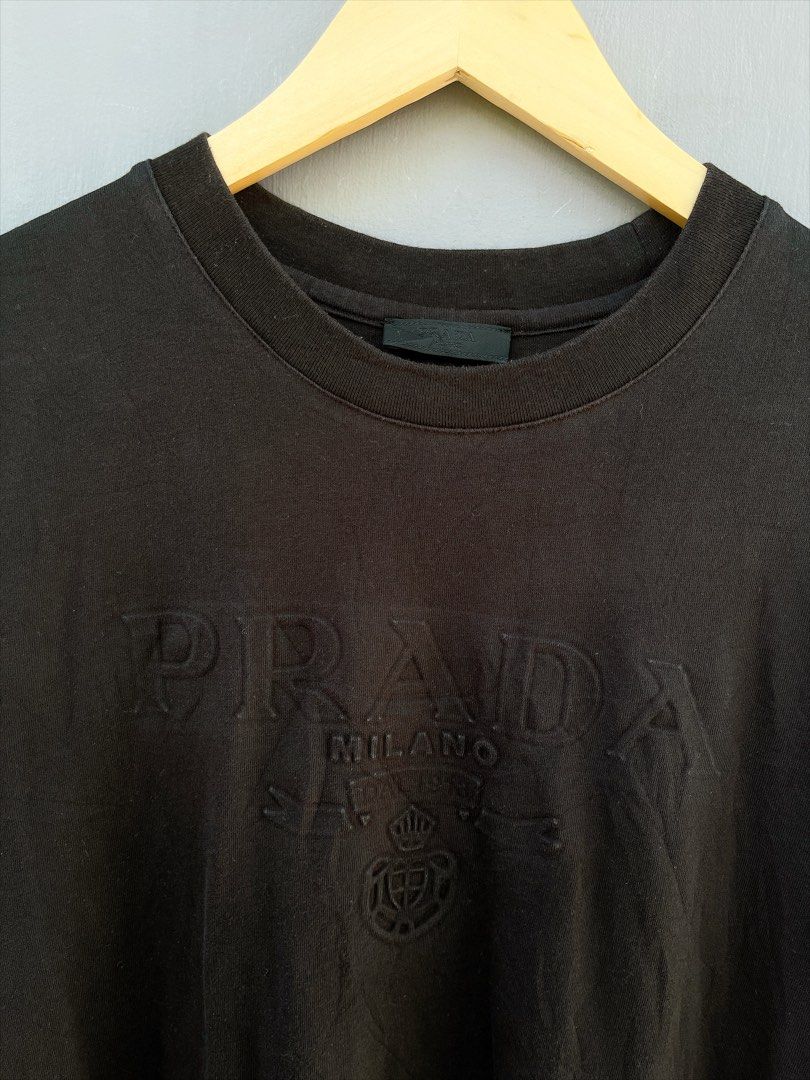 Prada Milano Embossed Logo T-Shirt Black (Category: Luxury Apparel) located in San Nicolas. Submitted by .luxfinds_0222 (Listing ID 1463322346, Image 2). Description: Size: M-L Width :21 Length :27.5 CR:9/10 Issue :NONE - Authentic Prada T-Shirt - Color: Black - Features embossed Prada logo, 'Prada Milano', and crest design - Made in Italy - Ideal for casual wear.