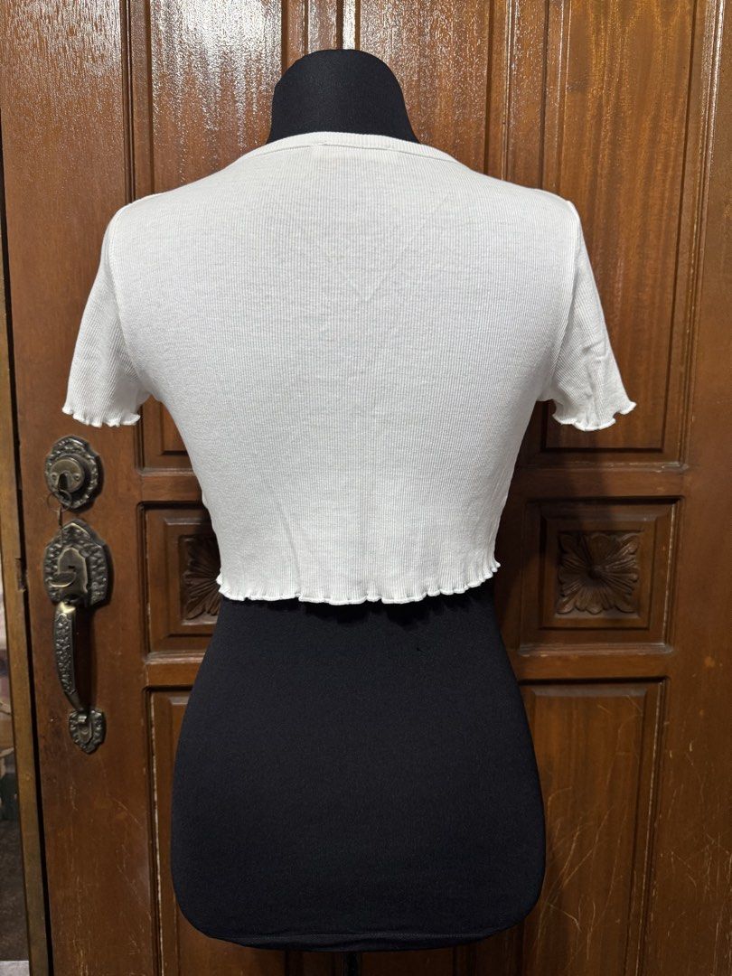 TERRANOVA White Ribbed Button Up Cropped Top Size M (Category: Shirts) located in Manila. Submitted by prelovedshopmnl (Listing ID 1463181292, Image 2). Description: - White ribbed crop top - Brand: Terranova - Short sleeves with lettuce hem detail - Button-up front - Versatile for layering or wearing alone - Size: Medium (M).