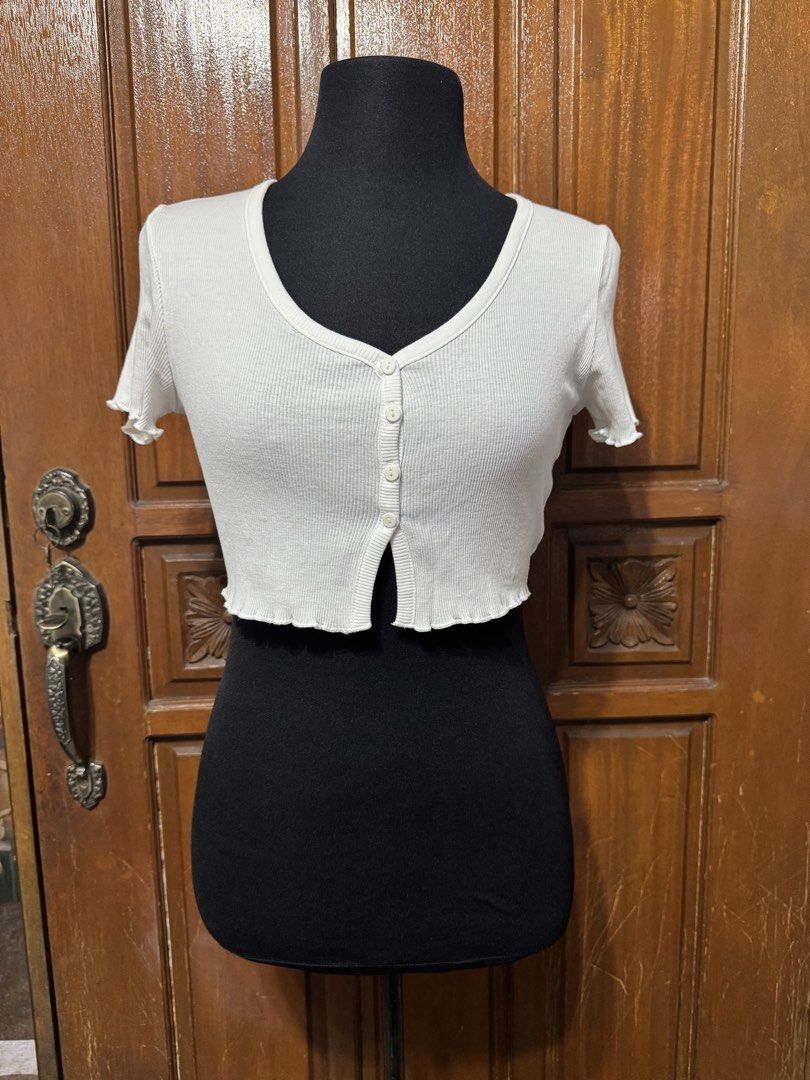 TERRANOVA White Ribbed Button Up Cropped Top Size M (Category: Shirts) located in Manila. Submitted by prelovedshopmnl (Listing ID 1463181292, Image 1). Description: - White ribbed crop top - Brand: Terranova - Short sleeves with lettuce hem detail - Button-up front - Versatile for layering or wearing alone - Size: Medium (M).