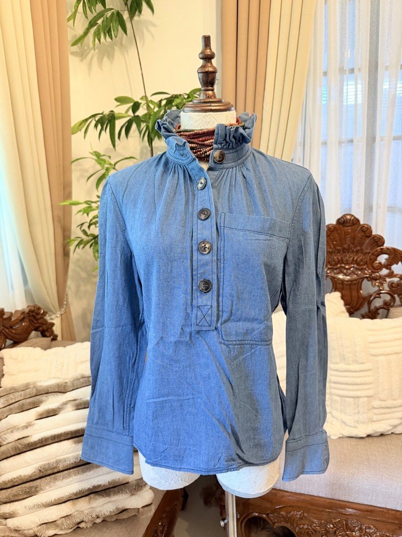 Tory Burch Chambray Ruffle Neck Blouse (Category: Blouses) located in Santiago. Submitted by yrellagnoihsaf (Listing ID 1463142371, Image 1). Description: - Brand: Tory Burch - Color: Blue Chambray - Size: 4 - Features: Ruffled high neck, button-up front, long sleeves with button cuffs, chest pocket - Origin: Made in China.