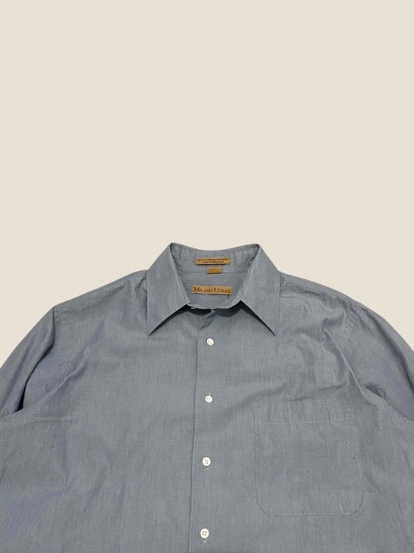 Vintage Milano Uomo Slate Blue Button-Down Shirt (Category: Formal Shirts) located in Santa Rosa. Submitted by revive.n.thrive (Listing ID 1463304901, Image 3). Description: A minimal essential tailored for an effortless preppy look and quiet luxury aesthetic. Rendered in a muted slate blue / chambray-style tone, this piece features a sharp pointed spread collar, clean front placket with pearl white buttons, and a single left chest pocket. Cut fr